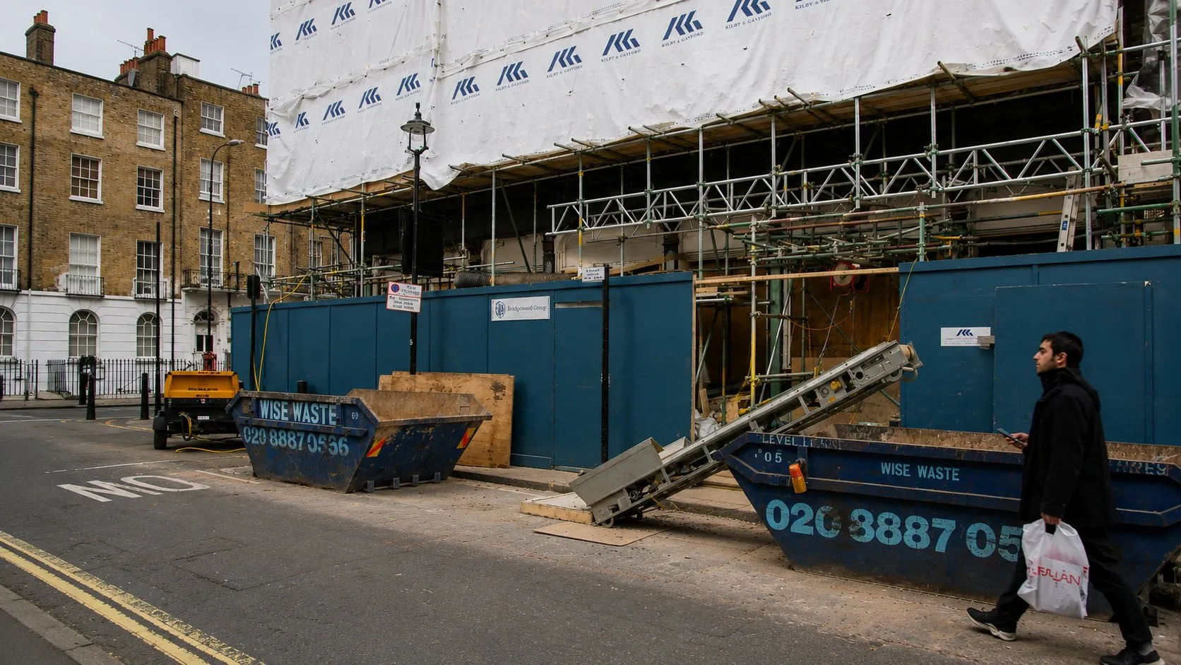 London street with site hoarding and a skip