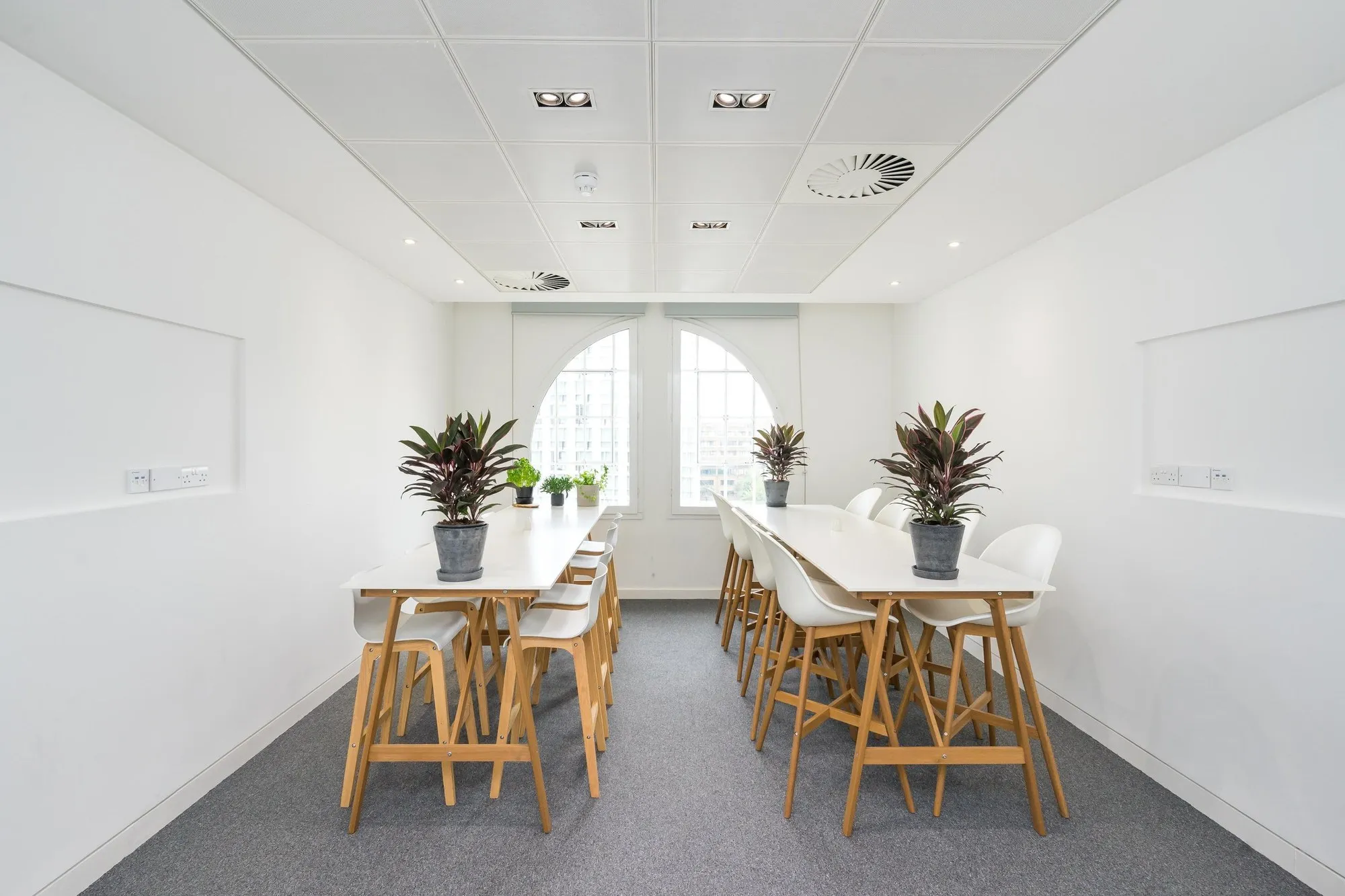 Breakout room at Beaumont House with high timber benches, white stools and plants under arched windows