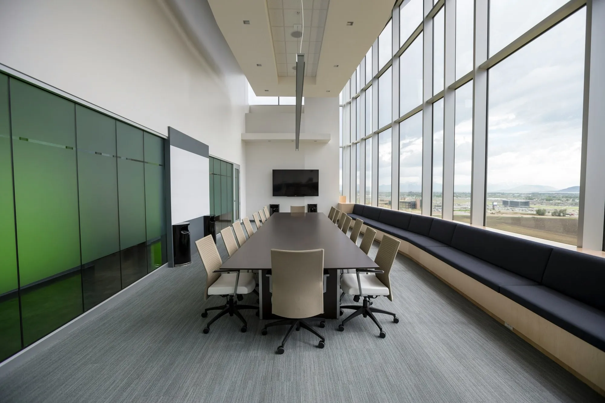 Boardroom with a long table, tinted glass partition wall, window bench and floor-to-ceiling glazing