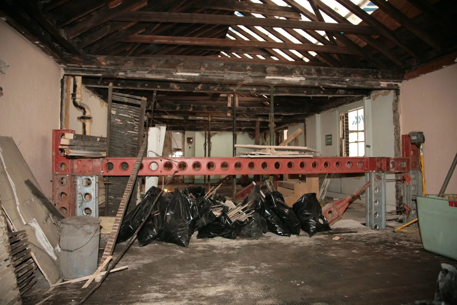 Stripped-out pub interior with exposed roof timbers, a new red steel beam and bagged waste on the floor