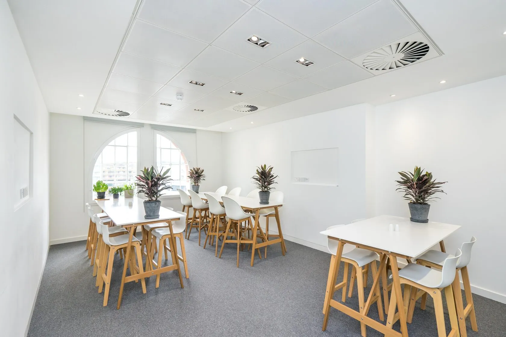 Finished breakout room at Beaumont House with white high tables, oak stools and an arched window