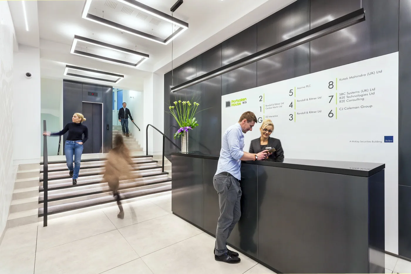 Rebuilt reception at Portsoken House, Aldgate, with a dark stone desk, lit stair and tenant directory