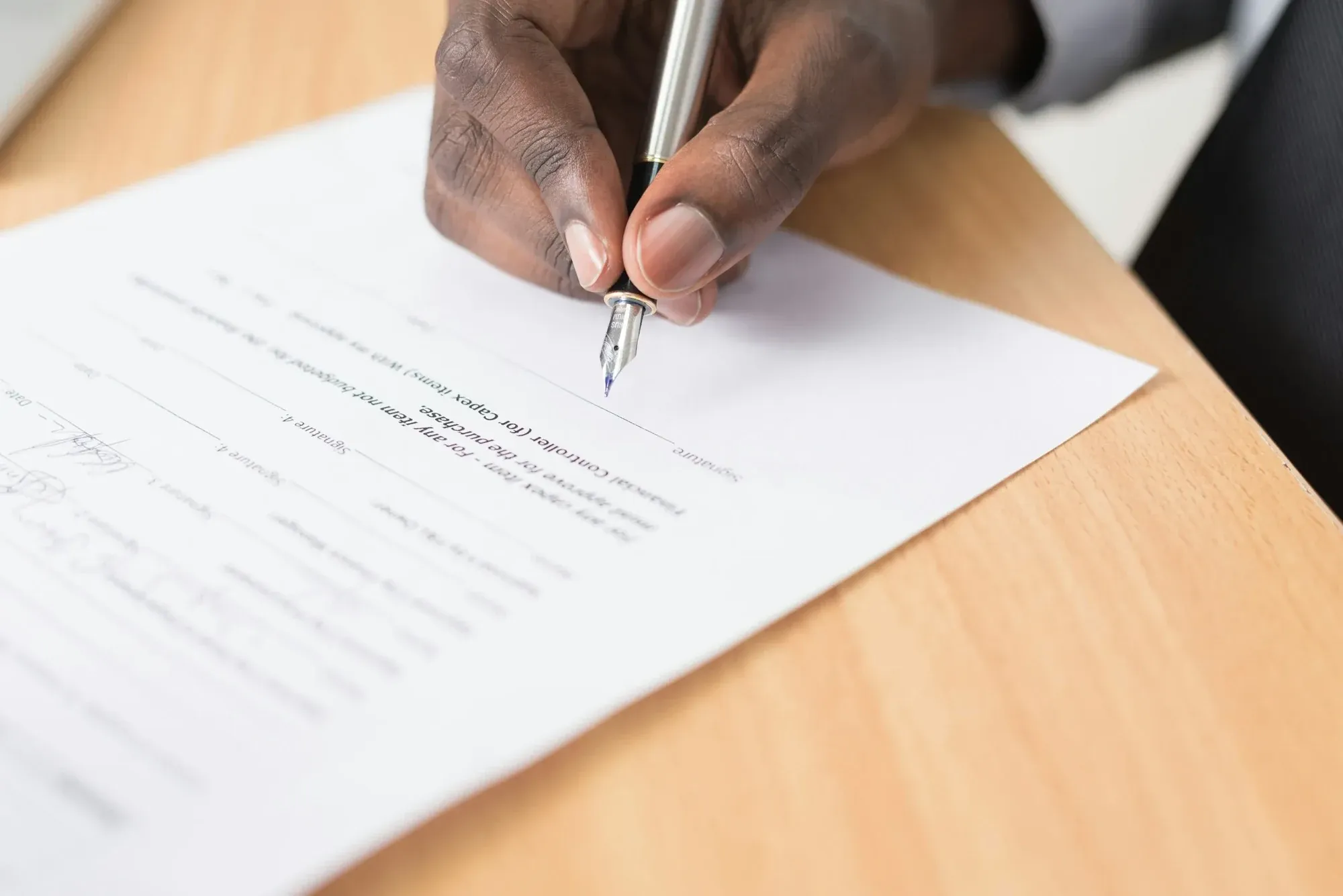 Hand signing a printed document with a fountain pen on a wooden desk