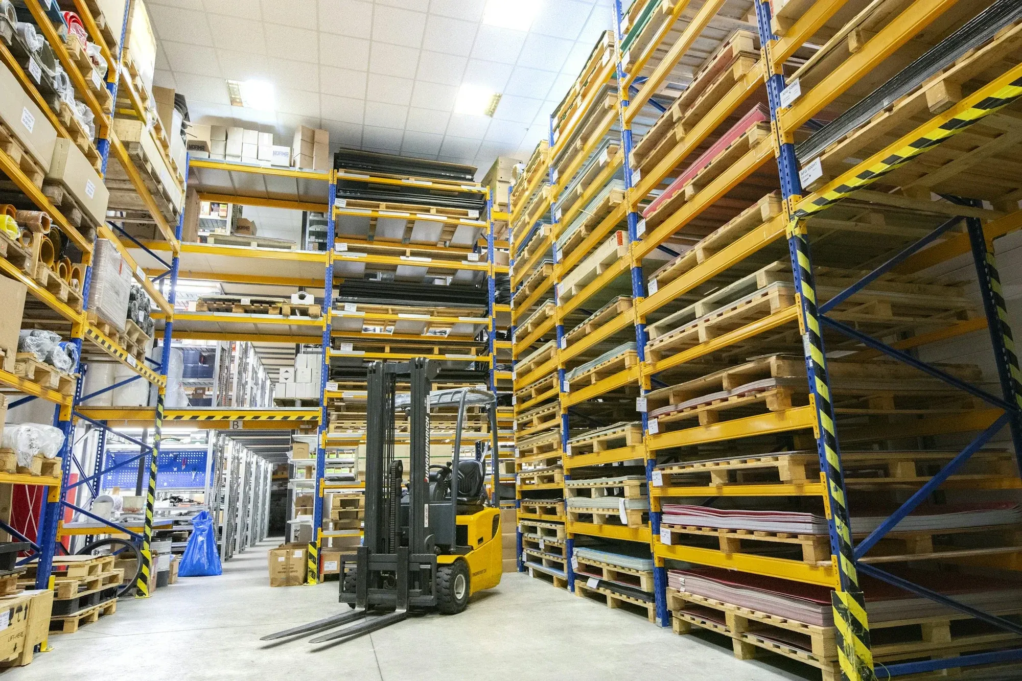 Forklift in a wide aisle between tall pallet racking in a warehouse